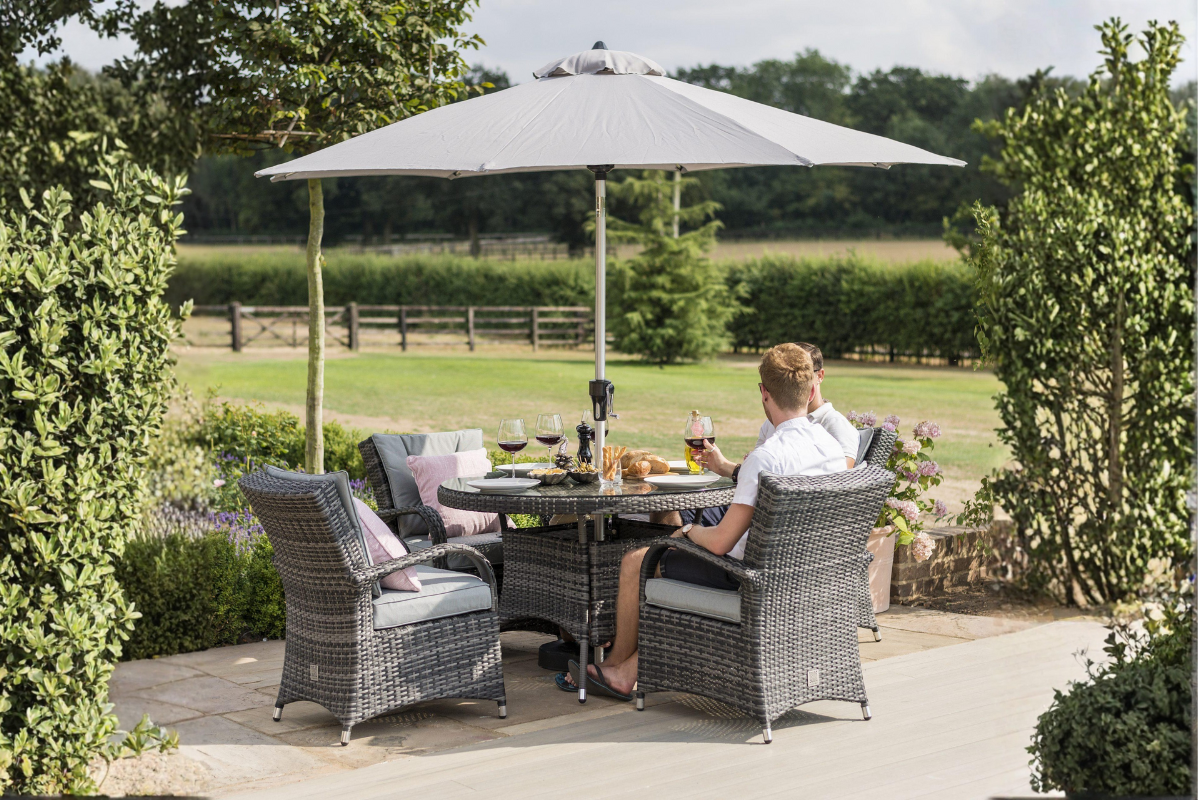A couple dining outdoors at a 4-seater rattan table under a patio umbrella, creating a cozy and elegant setting.
