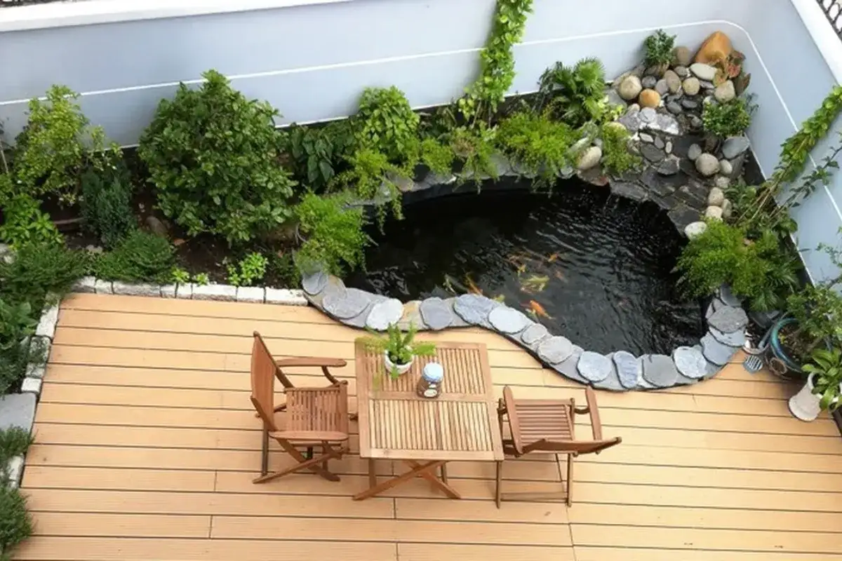 Hồ cá nhỏ trên sân thượng với cây xanh, viền đá và khu ngồi bằng gỗ