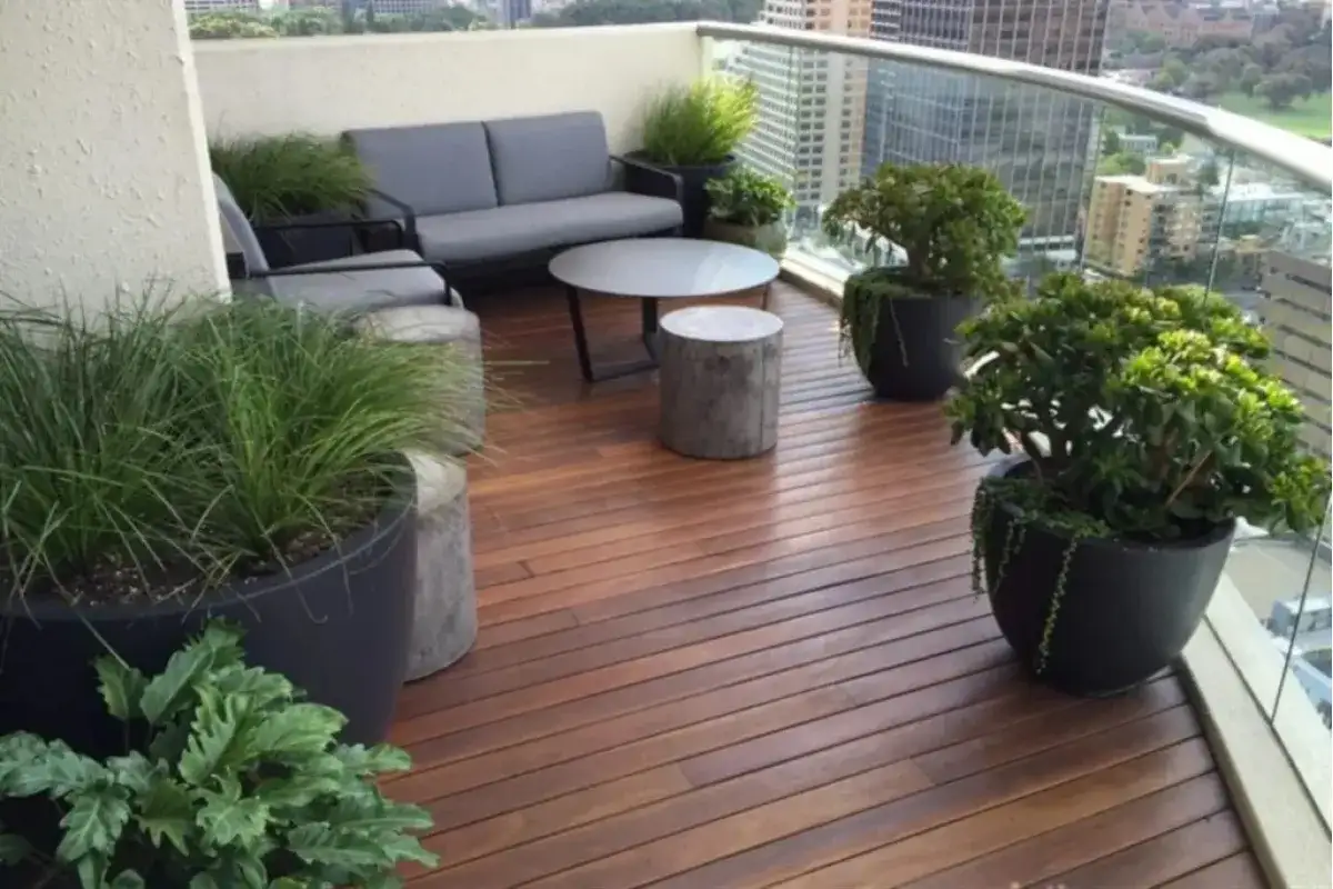 Ban công hiện đại lát sàn gỗ ngoài trời với sofa xám, bàn tròn và chậu cây xanh nhìn ra thành phố