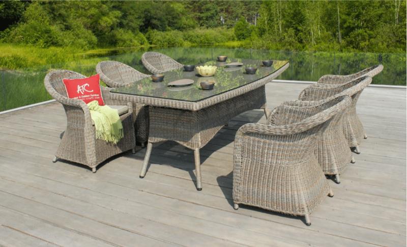 Outdoor wicker dining set with six chairs and a glass-top table on a deck, featuring an ATC pillow, overlooking lush greenery and a serene view