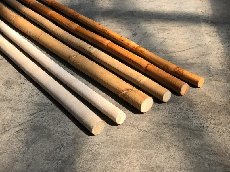 Bamboo poles arranged on a concrete floor, showing different sizes and shades of natural wood used for furniture or crafts